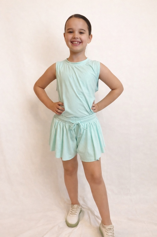 Young girl wearing a mint green sleeveless top and flowy skort with drawstring against a plain background