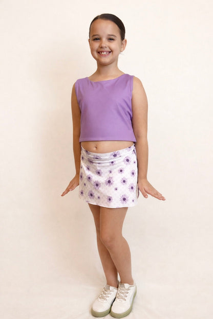 Young girl wearing a purple sleeveless top and floral skirt on a plain background